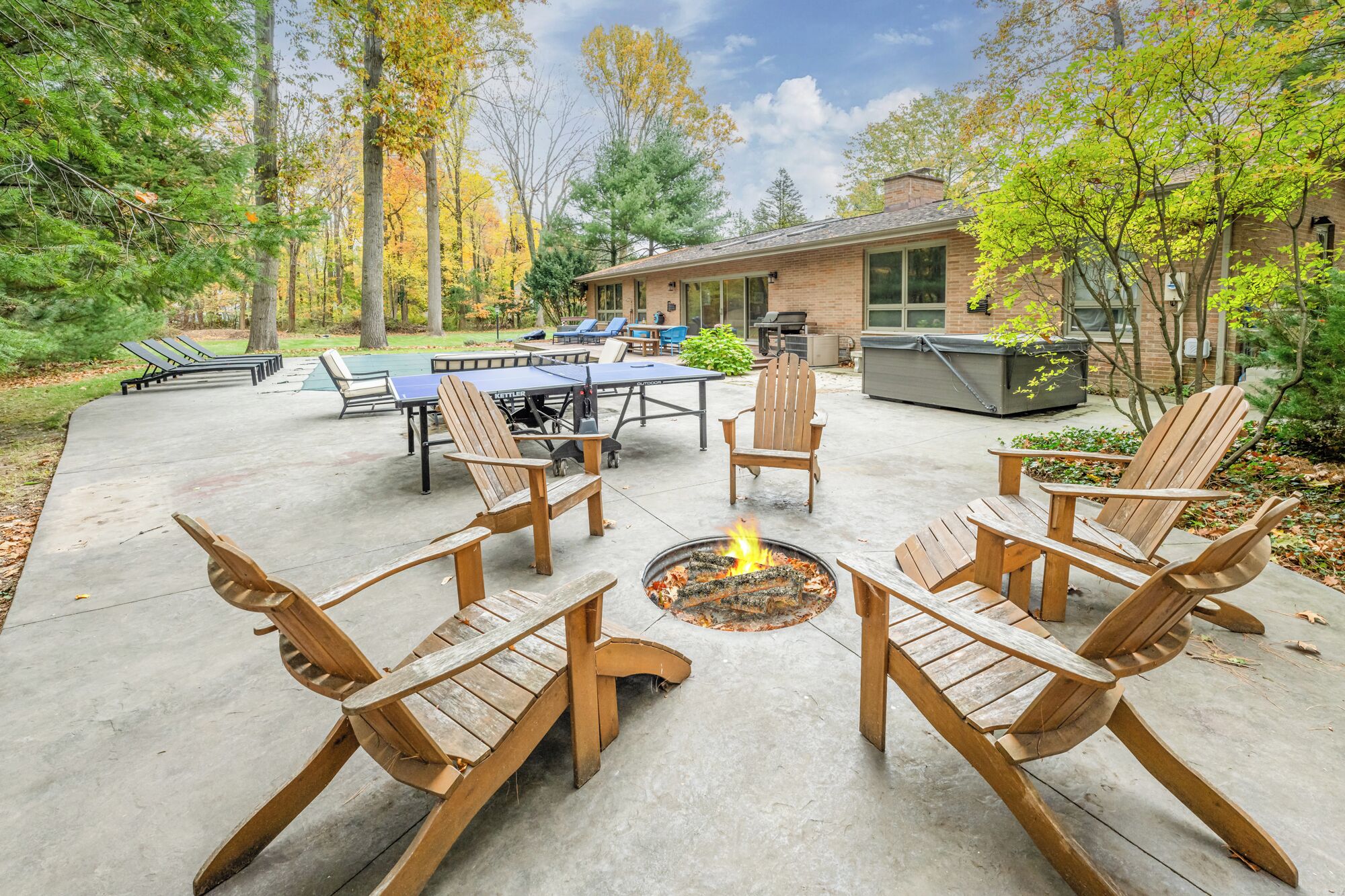 An outdoor patio with Adirondack chairs, a fire pit, and a ping pong table.