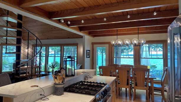 A modern kitchen with a central island, wooden ceiling, and large windows overlooking a body of water. - Private Lakefront Estate with 180 Degree Views (Raymond)