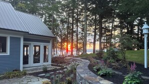A house with a stone pathway leading to a deck, surrounded by a garden with various plants and flowers. - Private Lakefront Estate with 180 Degree Views (Raymond)