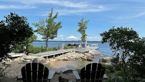 A lakeside deck with Adirondack chairs, a small table, and a white umbrella. - Private Lakefront Estate with 180 Degree Views (Raymond)