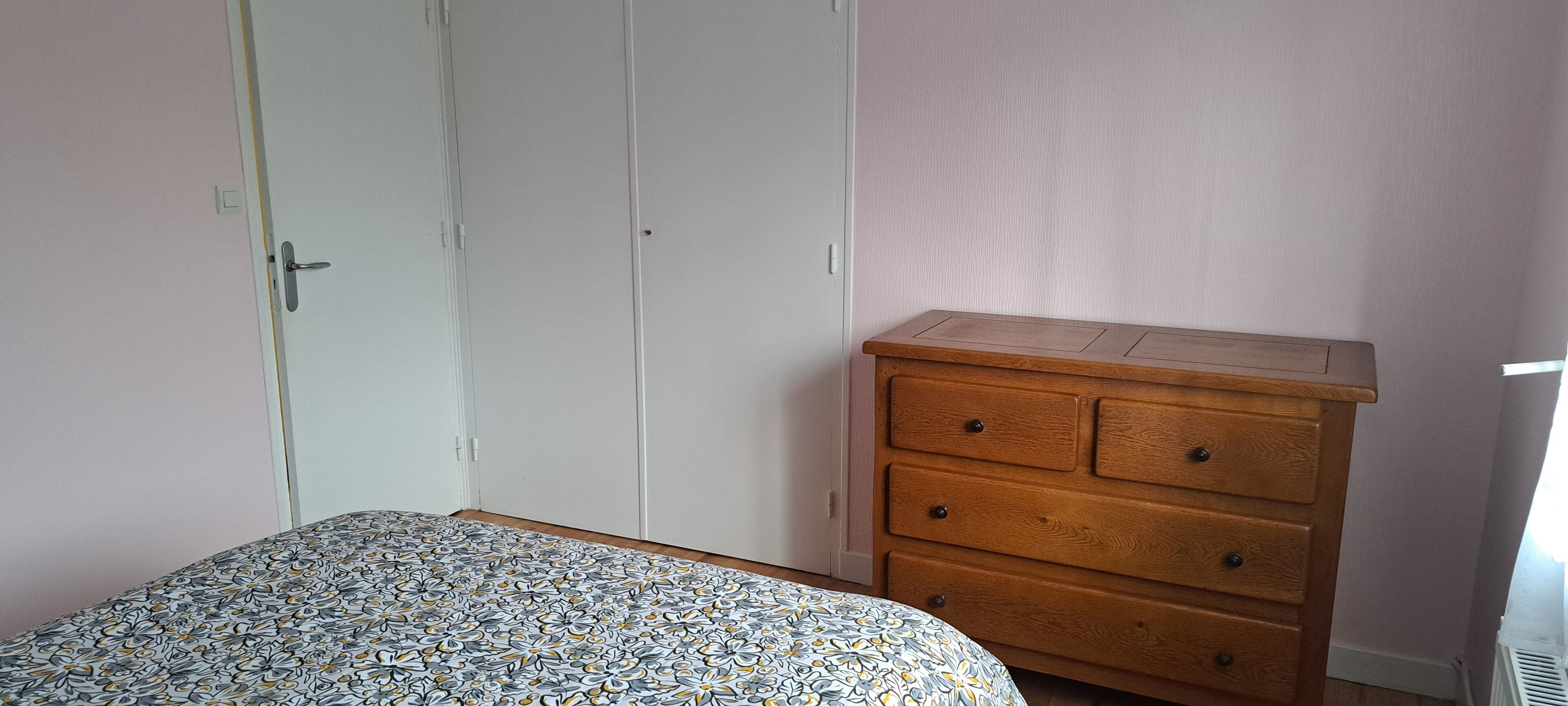 Een slaapkamer met een bed, een houten dressoir en een witte kledingkast.