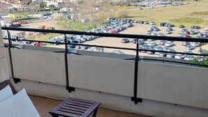 Un balcon avec un canapé, une petite table et un globe terrestre. Le balcon donne sur un parking et offre une vue lointaine sur des bâtiments et des arbres.