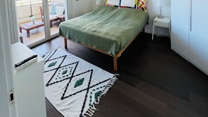 Une chambre comprenant un lit, un petit bureau, une table de chevet, une armoire et une porte-fenêtre coulissante donnant sur un balcon.