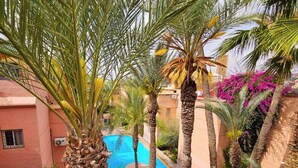 A pool surrounded by palm trees and a building with a pink facade. - Beautiful 4 Bedroom Riad with Rooftop Terrace, Pool & Airport Shuttle Marrakech (Marrakesh)