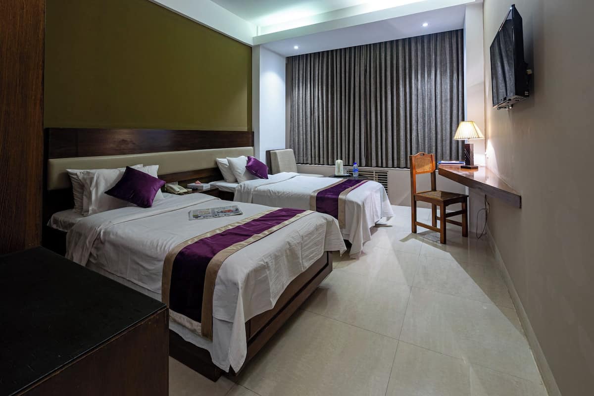 A hotel room with two beds, a desk, a chair, a TV, and a window with curtains.