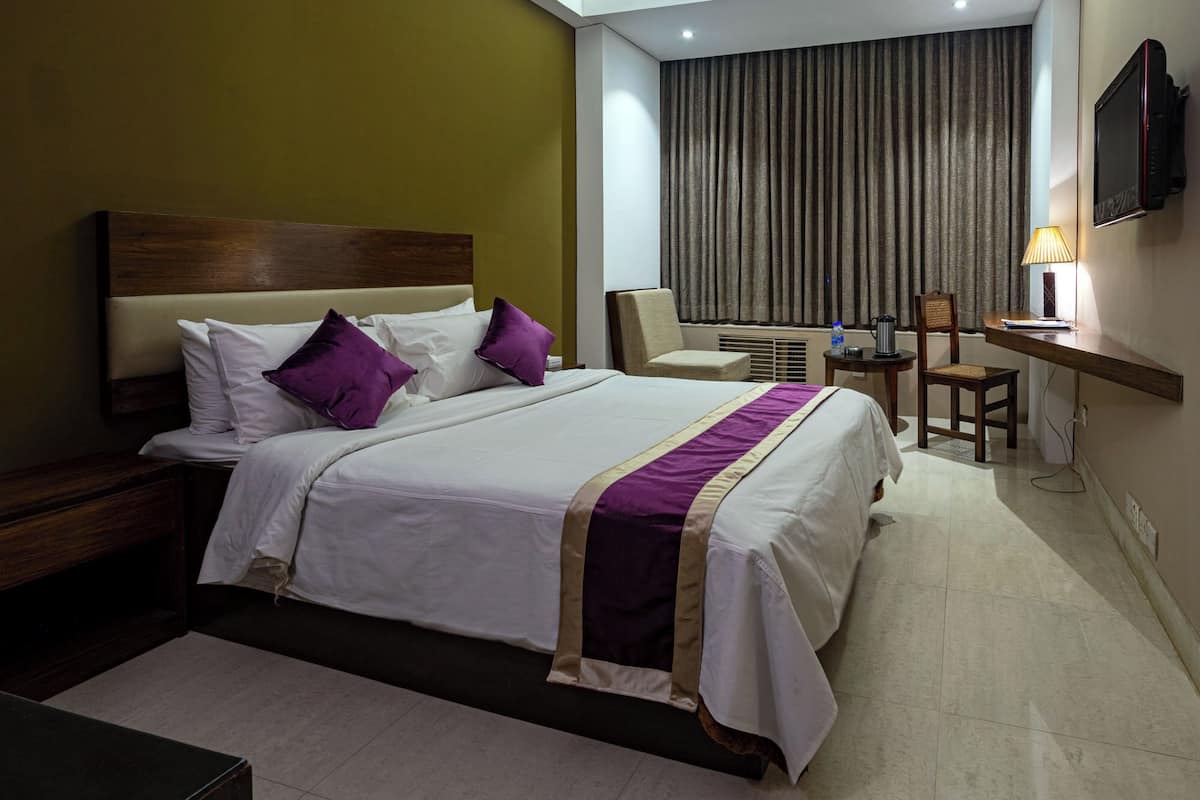 A hotel room with a large bed, a desk, a chair, a TV, and a window with curtains.