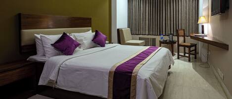A hotel room with a large bed, a desk, a chair, a TV, and a window with curtains.