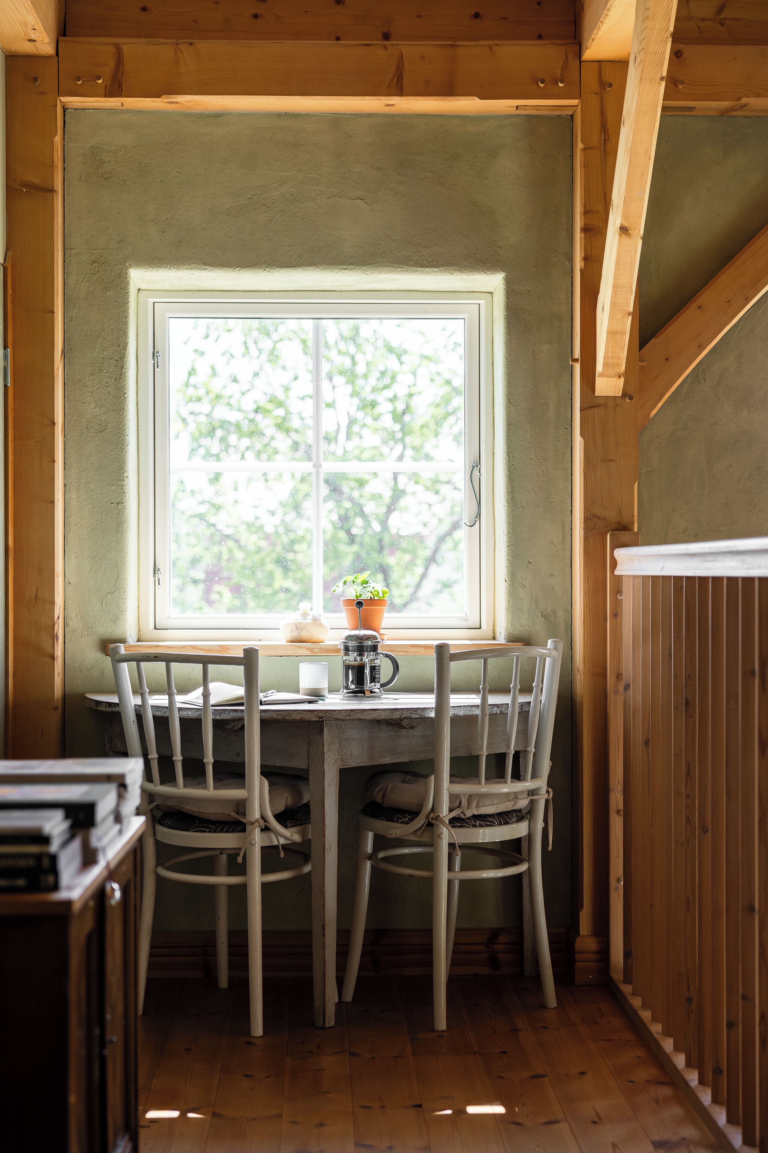 A wooden interior with a table and chairs, a window with a view of trees, and a radiator.