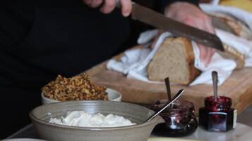 Una persona cortando pan sobre una tabla de madera, con diversos alimentos y utensilios a su alrededor.