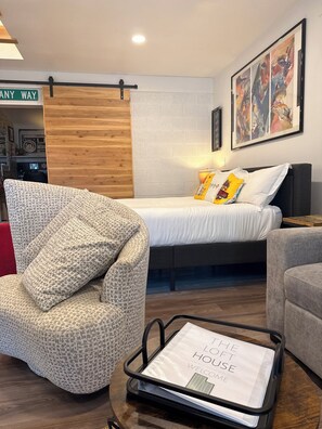 A modern bedroom with a bed, a chair, a bedside table, and a wall-mounted artwork.