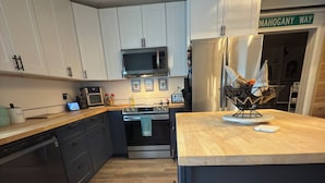 Una cocina moderna con armarios blancos, encimera de madera, horno empotrado, microondas y refrigerador.