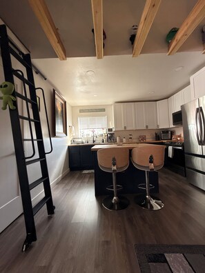 A modern kitchen with white cabinets, a stainless steel refrigerator, and a wooden ceiling.