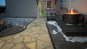 Una casa con un camino de piedra que lleva a la puerta principal, un hogar a leña y una pequeña terraza.