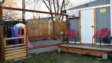 A backyard with a play area, including a slide and swings, and a small deck with chairs.