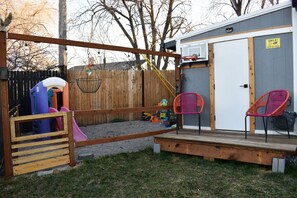 Ein Garten mit Spielbereich, darunter eine Rutsche und Schaukeln, sowie eine kleine Terrasse mit Stühlen.