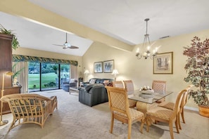 A spacious living area with a glass dining table, wicker chairs, a sofa, and a ceiling fan.