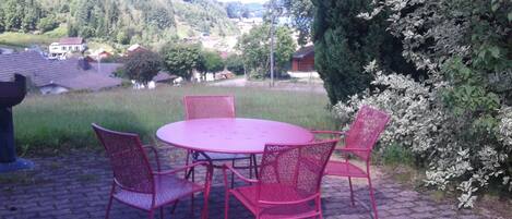 A round table with four chairs, a brick pathway, and a view of houses and trees in the background.