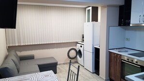 A compact kitchen with a washing machine, a refrigerator, and a dining area with a table and chairs. - Apartment for guests Iva (русе)