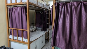 Ett sovsalsrum med våningssängar, lila gardiner och en vit madrass på den nedre våningssängen.
