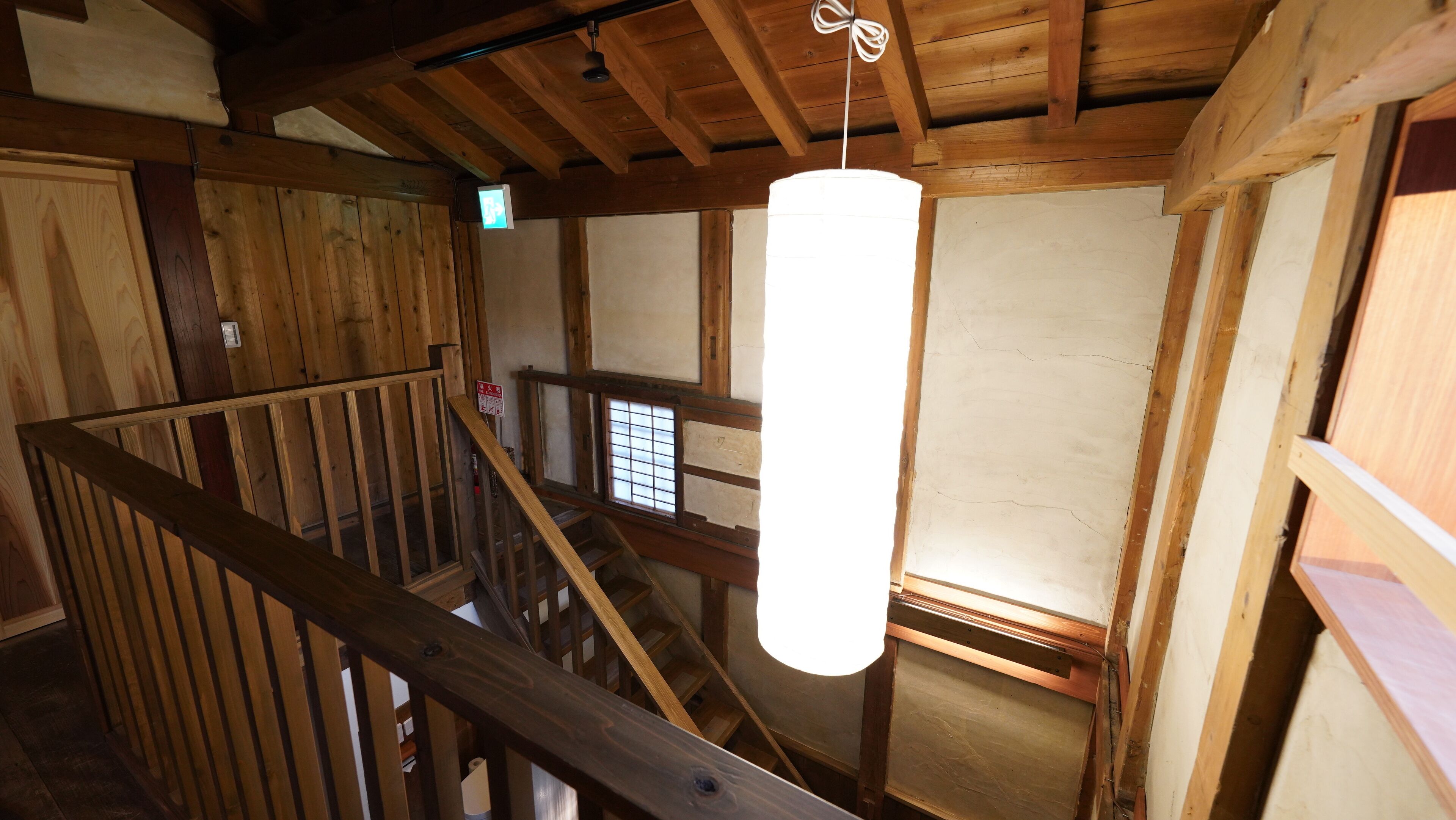 A wooden interior with a staircase, a hanging light fixture, and a window with a grid pattern.