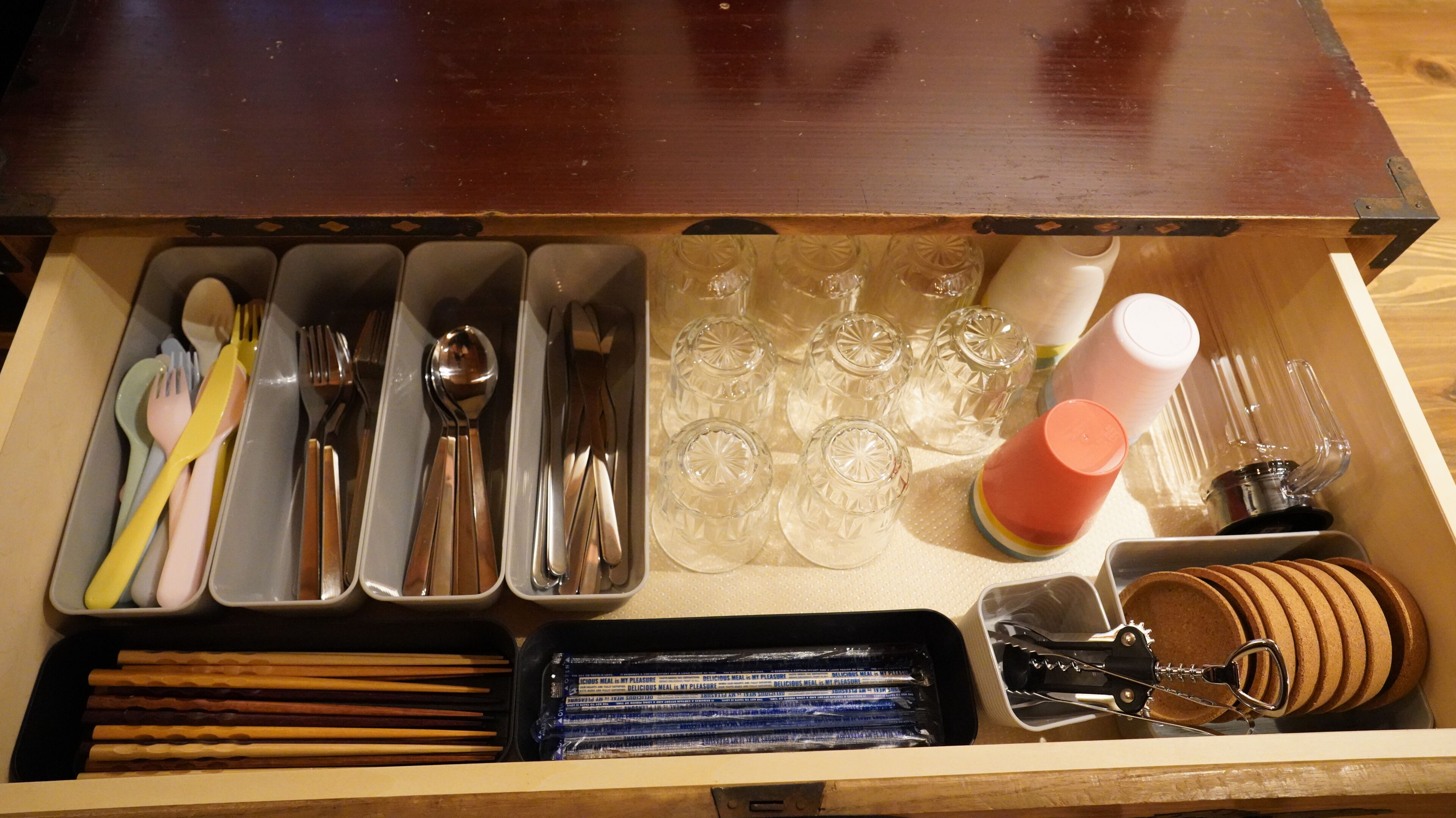 Un cajón con cubiertos, vasos y un sacacorchos.