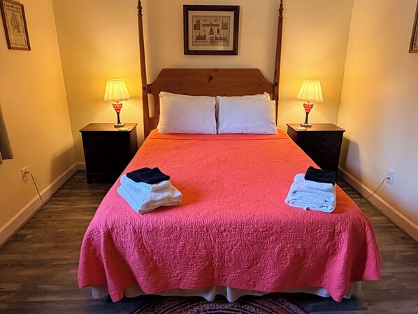 A double bed with a pink bedspread, two nightstands with lamps, and folded towels on the bed.