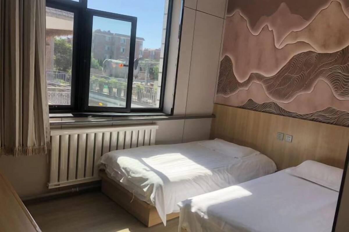 A bedroom with two beds, a window with a view of buildings, and a radiator.