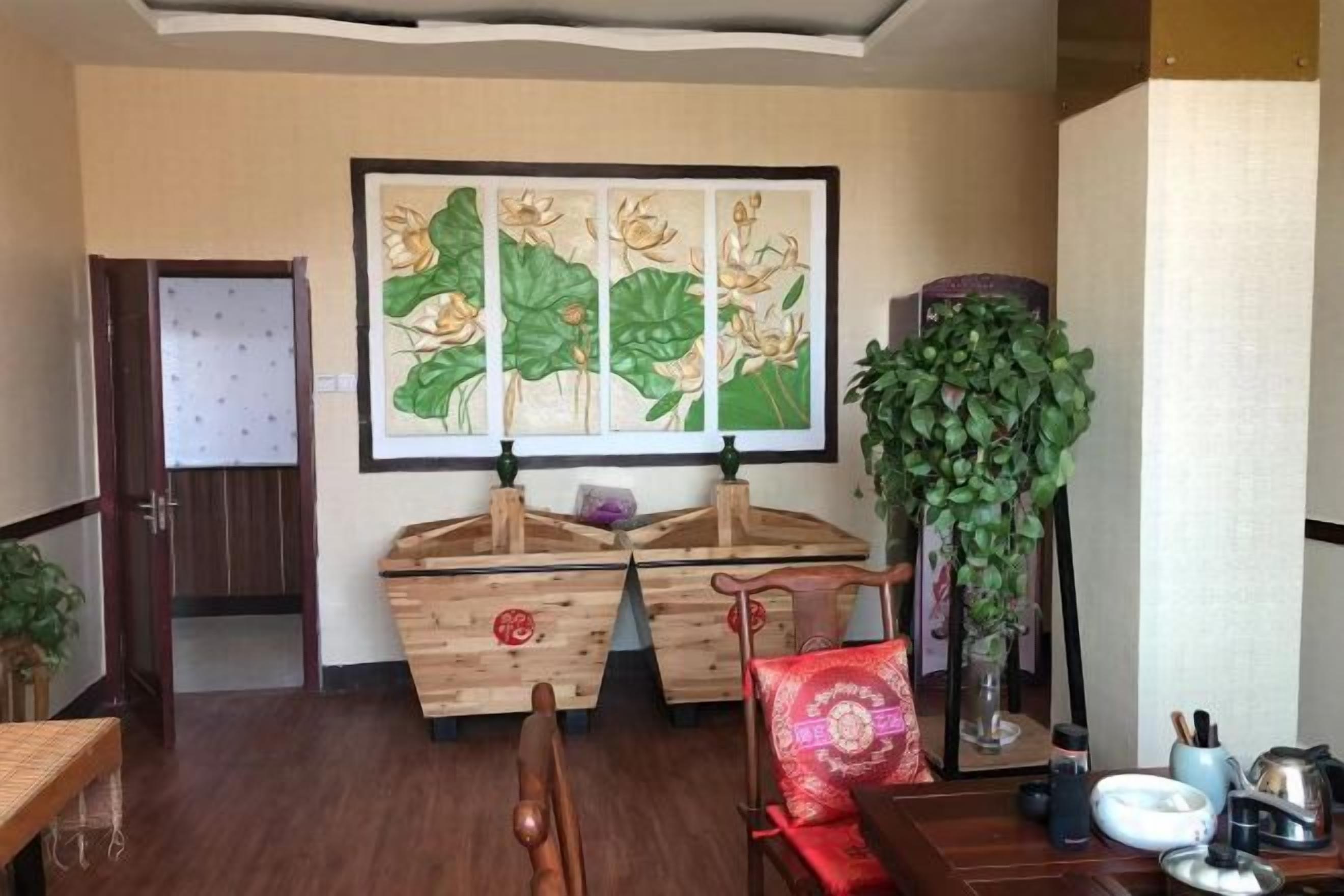 A room with a wooden cabinet, a painting, a tall plant, and a dining table with chairs.