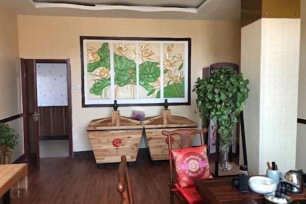 A room with a wooden cabinet, a painting, a tall plant, and a dining table with chairs. - Baiyangdian Weinan Hotel (Anxin)
