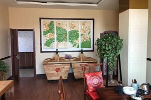 A room with a wooden cabinet, a painting, a tall plant, and a dining table with chairs.