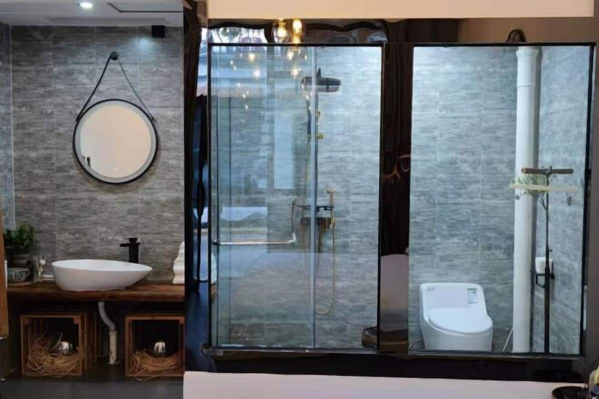 A modern bathroom with a glass-enclosed shower, a round mirror, and a white sink.