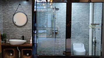 A modern bathroom with a glass-enclosed shower, a round mirror, and a white sink.