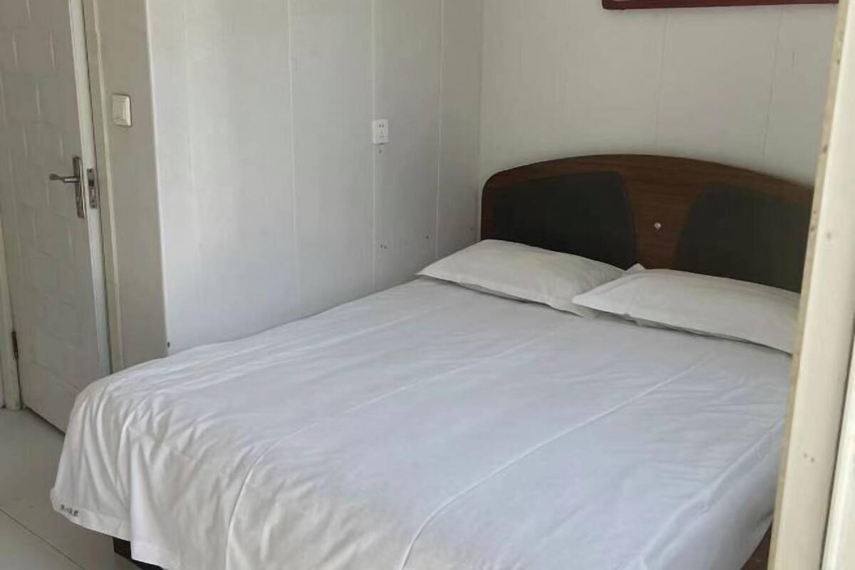 A single bed with white bedding in a room with white walls and a wooden headboard.