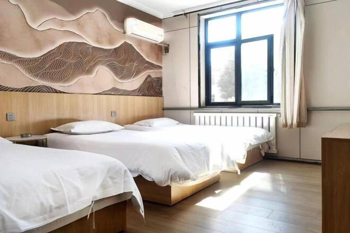A hotel room with two beds, a large window, and a unique wall design.