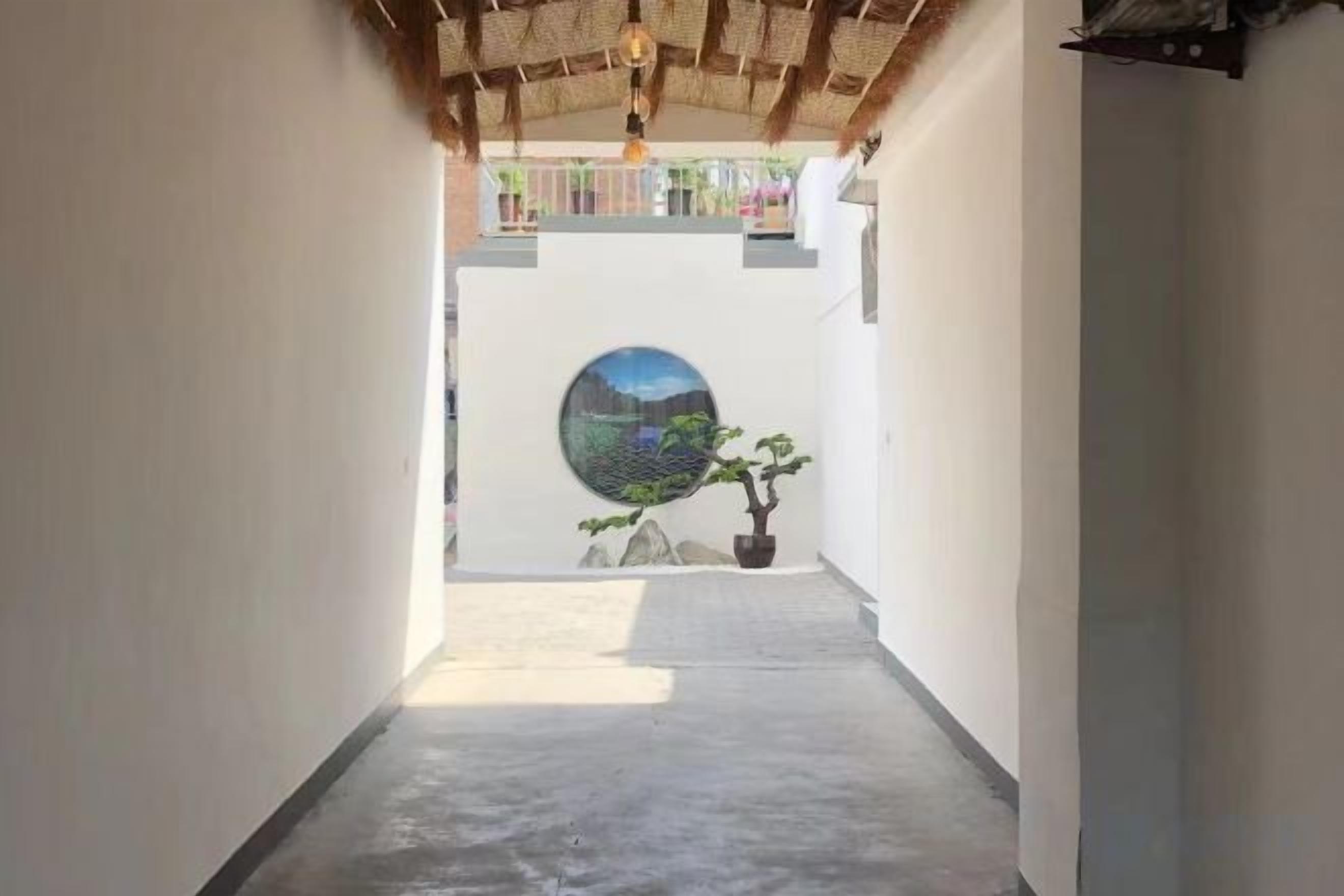 A narrow corridor with a concrete floor, a circular wall art, and a potted plant.