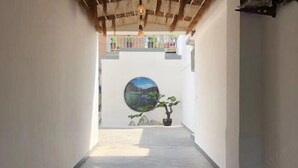 Un couloir étroit avec un plafond en chaume, une fenêtre circulaire donnant sur un paysage et une plante en pot.