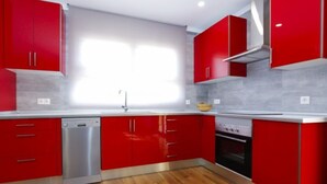 Une cuisine moderne avec des meubles rouges, un lave-vaisselle en acier inoxydable et un four encastré.