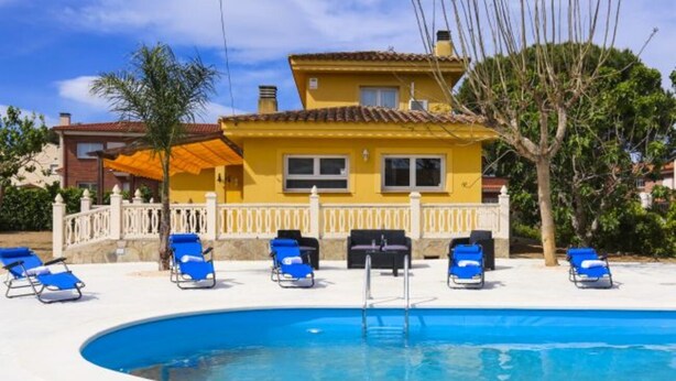 Un espace piscine avec des chaises longues bleues et un bâtiment jaune en arrière-plan.