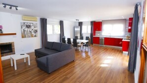 Un grand espace de vie comprenant un canapé, une table à manger et des chaises. Il y a également un coin cuisine avec des placards rouges et une fenêtre.