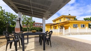 Une terrasse extérieure avec une table et des chaises, un barbecue et un bâtiment jaune en arrière-plan.