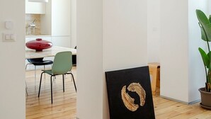 Un interior moderno con suelo de madera, una zona de comedor con un cuenco rojo y una obra de arte negra con diseño dorado.
