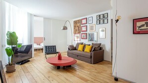 Una sala de estar moderna con un sofá, una mesa de centro roja, una silla negra y una planta en maceta.