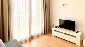 A room with a TV on a white cabinet, a clock on the wall, and a window with curtains. - Global Port Global, en el Centro de Cambrils 40 (Cambrils)