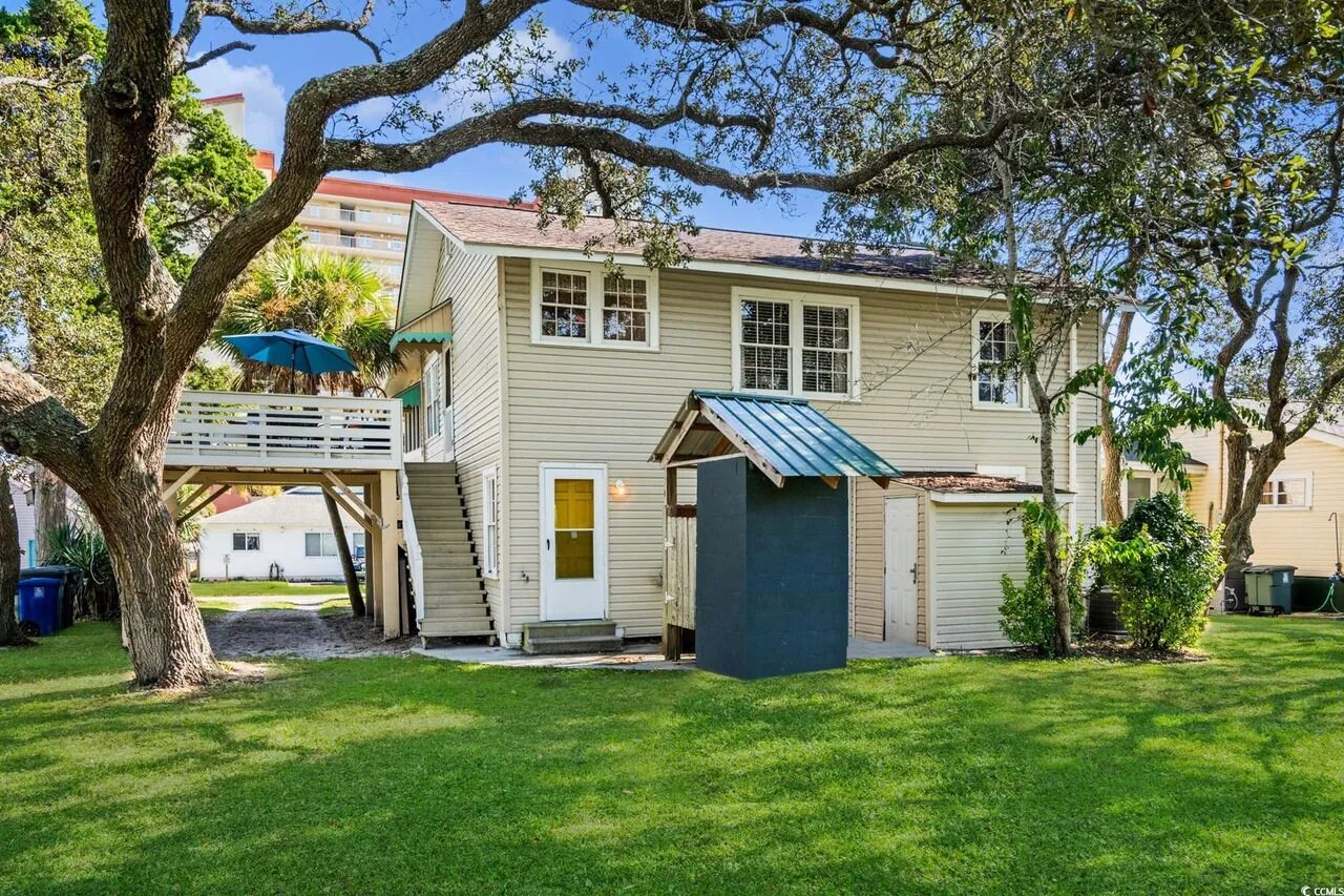 A two-story house with a covered porch, a small shed, and a tree in the yard.