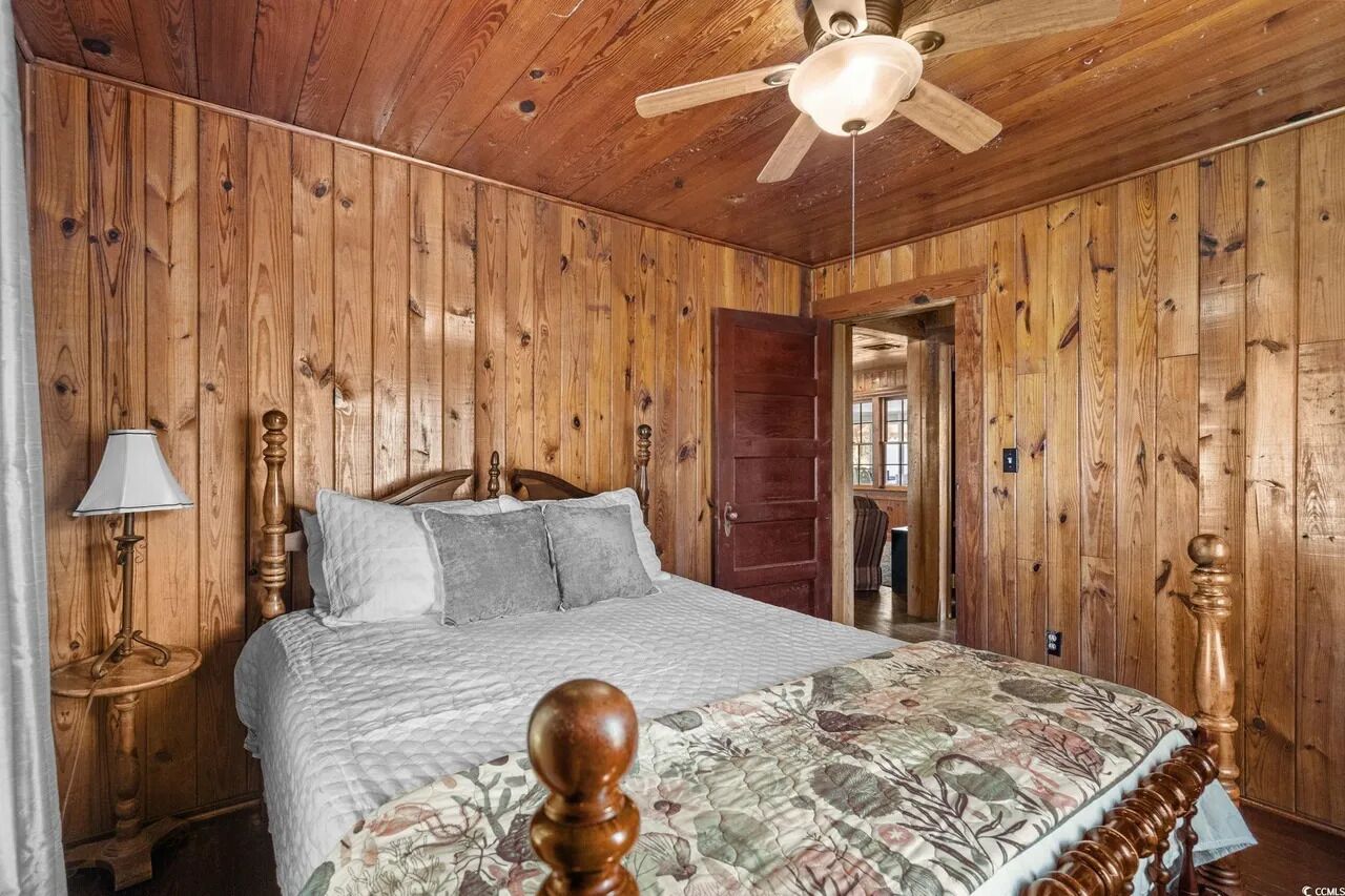 A wooden-paneled bedroom with a bed, a nightstand, a lamp, and a ceiling fan.
