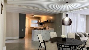 Een moderne keuken met een centraal eiland, een eethoek met een ronde tafel en stoelen, en een zithoek met een bank en gordijnen.