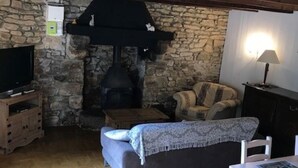 A cozy living room with a stone fireplace, a sofa, a television, and a dining table. - Traditional Breton Penty in the heart of Brittany... (Lanrivain)