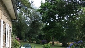 A patio with a table and chairs, surrounded by a well-maintained lawn and flowering plants. - Traditional Breton Penty in the heart of Brittany... (Lanrivain)