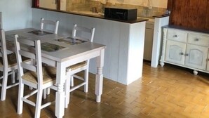 A dining area with a white table and chairs, a kitchen with a window, and a wooden ceiling. - Traditional Breton Penty in the heart of Brittany... (Lanrivain)