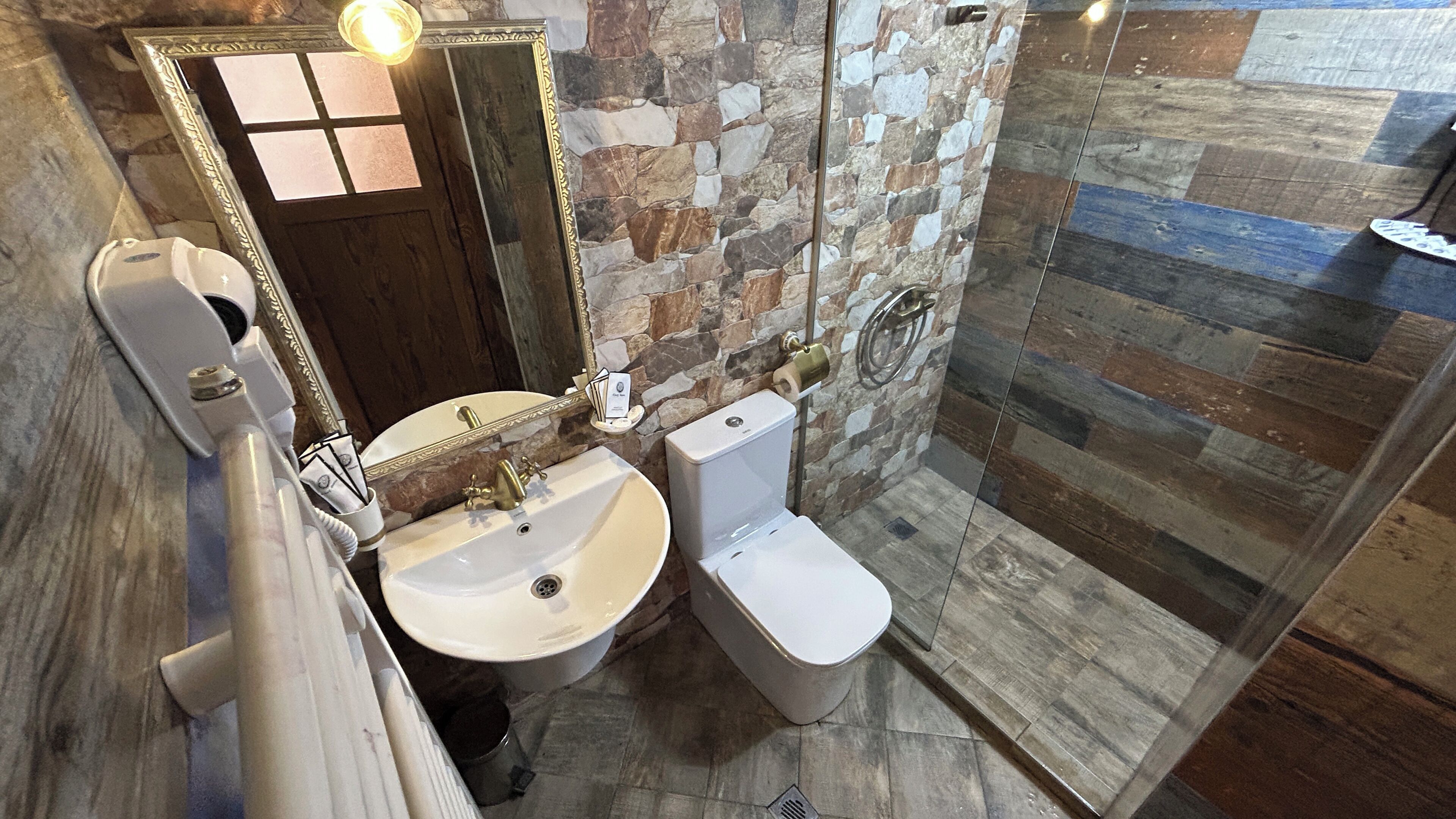 A bathroom with a stone wall, a sink, a toilet, and a glass shower enclosure.